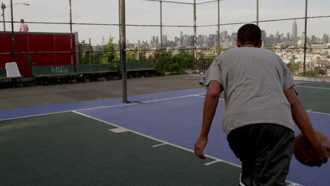 kid driving to basket and scoring finger-roll layup - outdoor basketball court in New Jersey with Manhattan skyline through fence