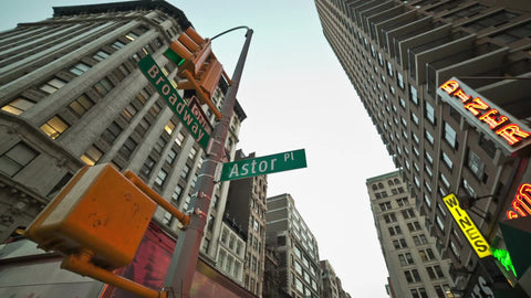 Astor Place and Broadway signs with taxis and cars driving in Manhattan traffic during the day in NYC