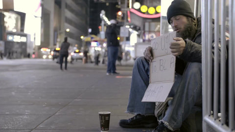 tragic homeless man with humorous sign in Times Square at night