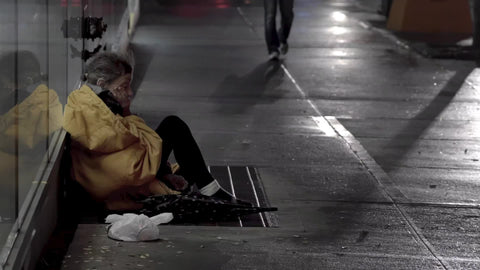 homeless woman sitting on sidewalk while pedestrians walk by people ignoring lady on busy night in Manhattan New York City