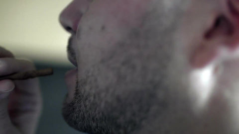 profile view of man pulling from blunt - smoking marijuana - hitting that herb