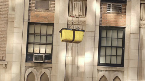 bucket lowering down side of building to construction workers at site in hardhats in NYC
