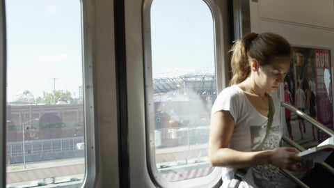 pretty woman standing, riding elevated subway train past Arthur Ashe Stadium where US Open is hosted in Queens