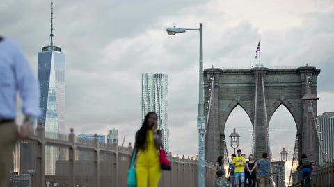 Brooklyn Bridge with Freedom Tower view - woman on cell phone talking on summer day crossing in NYC