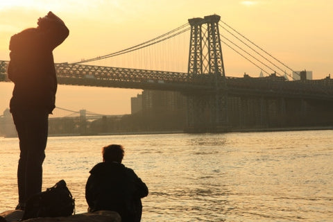 Manhattan Bridge at sunset - people enjoying view of beautiful orange sky over East River from Brooklyn