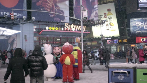people walking in the snow in Times Square - cartoon characters costumes and subway station lights - snowing at night in New York City
