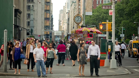 people walking on 5th Ave in Manhattan with clock in background