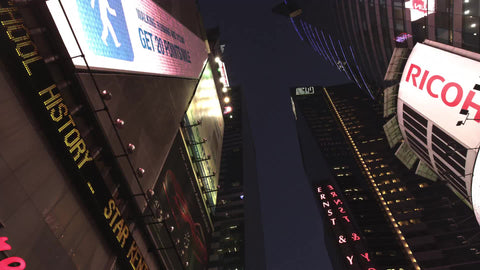 upward angle of tall buildings driving through Times Square at night with bright lights and ticker in NYC
