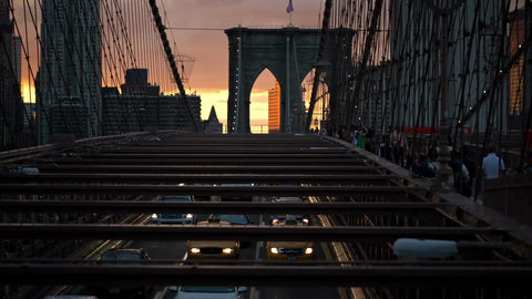 Brooklyn Bridge interior view over cars driving slowly in traffic below at sunset in NYC