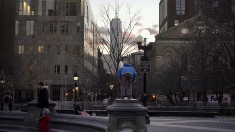 boy standing atop Washington Square Park circle with Freedom Tower at sunset on winter day
