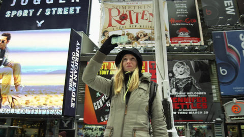 tourist woman taking pictures and video recording Times Square in winter - snowing in Manhattan on cold day