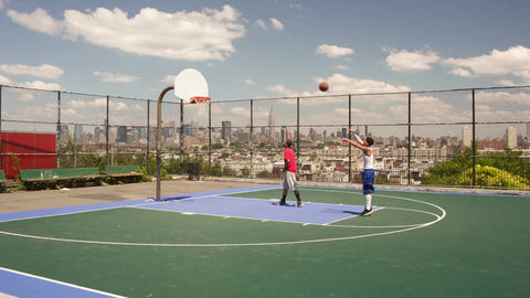 kid shooting and scoring free throw shot in game of 1 on 1 basketball with view of Manhattan skyline through fence on summer day