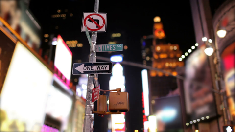 Times Square sign with billboards, bright lights and ads out of focus in background in New York City at night
