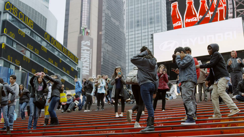 red stairs in Times Square crowded with kids posing for pictures - tourists visiting New York City on cold winter day in 4K slow motion
