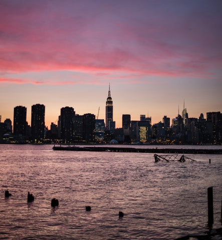 Empire State Building night lights in Manhattan skyline view from Brooklyn from across the East River with wooden dowels in the water at colorful sunset